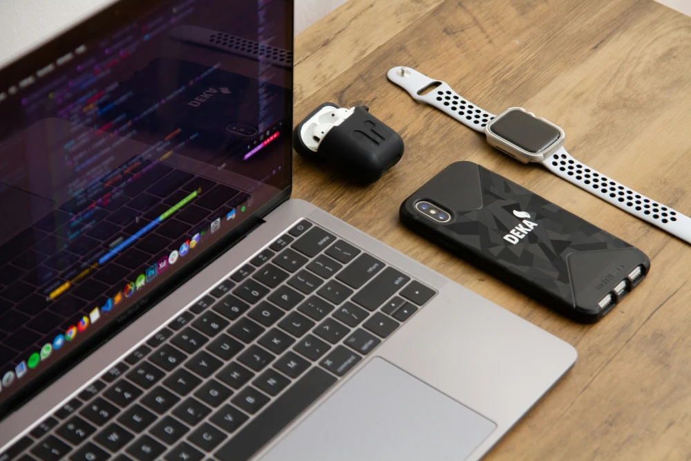 Laptop showing code next to a phone and smartwatch